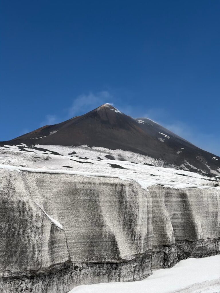 Craterul Vulcanului Etna fumegând, cu munți de zăpadă pe traseu